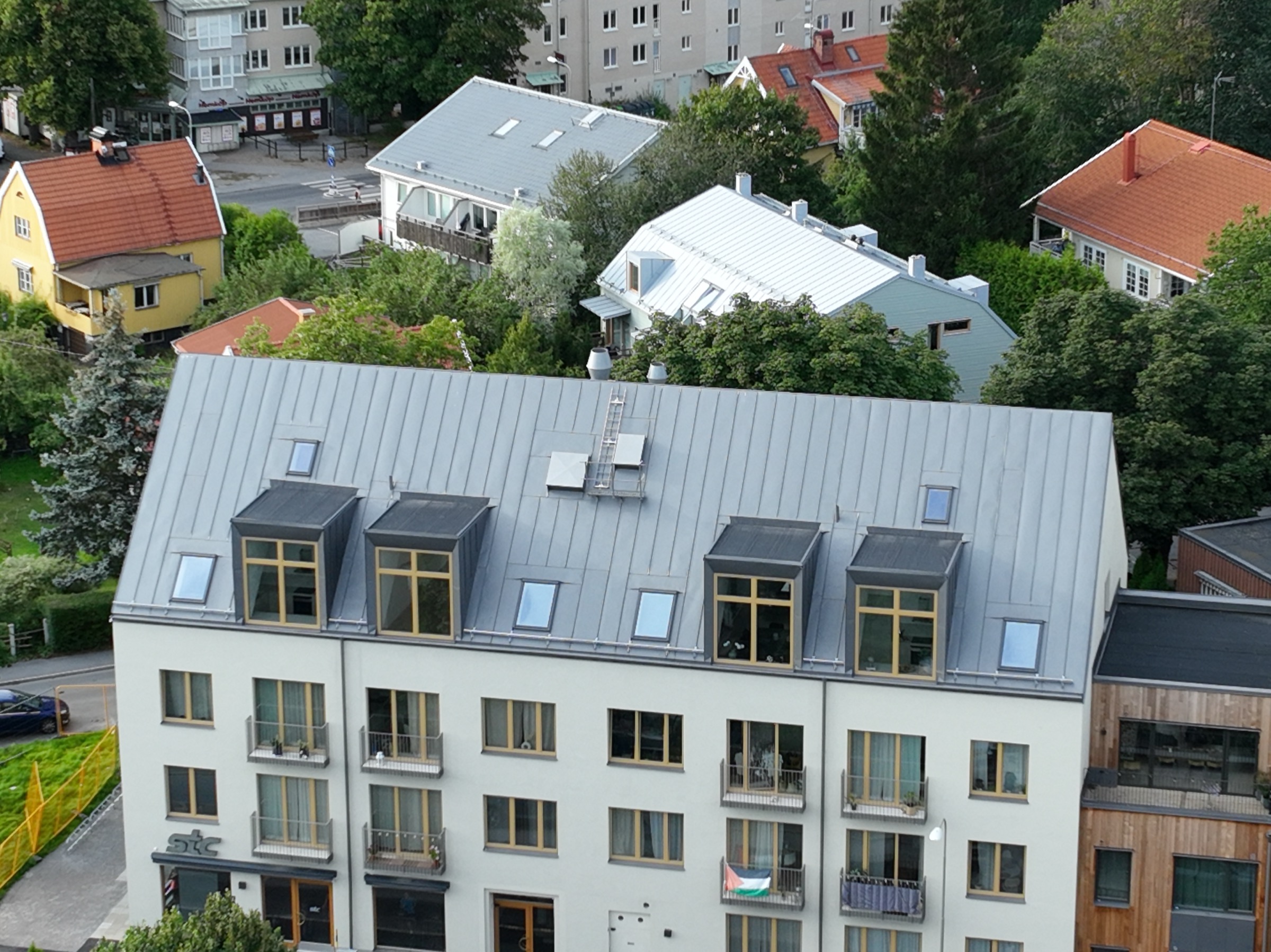 Bandtäckning — drönarvy över lägenhetsbyggnad med komplett falsplåts-tak, takkupor och nya takfönster